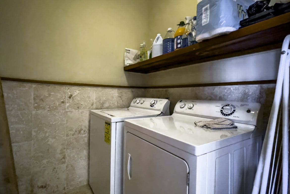buyDRproperty Laundry room with a white washer and dryer, cleaning supplies on shelf. Sosua Real Estate
