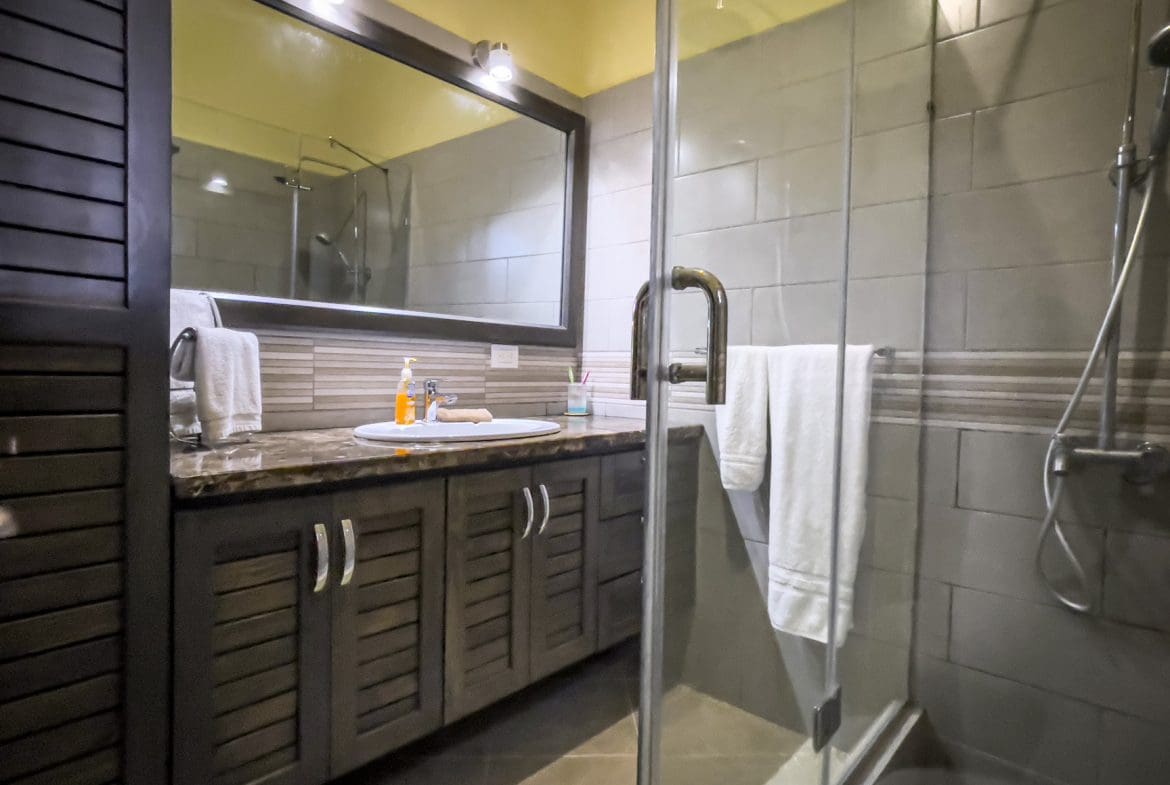 buyDRproperty Bathroom in a stunning 2 bedroom villa. Dark wood vanity, glass shower, and white towels. Sosua Real Estate