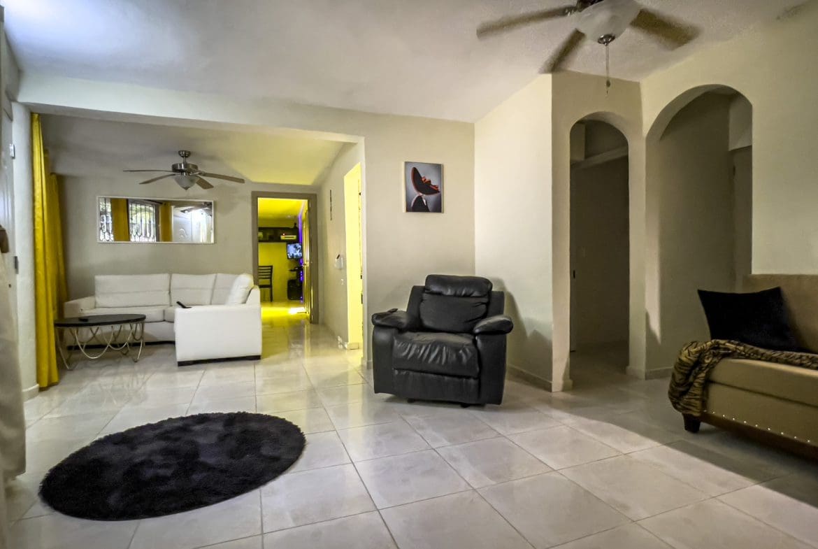 buyDRproperty Living room for sale in a smart home. Features include a black leather recliner and tiled floors. Sosua Real Estate