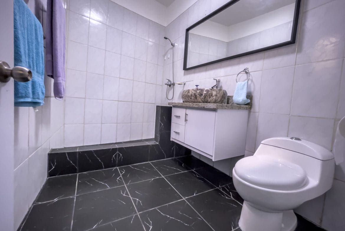 buyDRproperty Modern bathroom with black marble-style floor, white tiles, and a floating vanity. Sosua Real Estate
