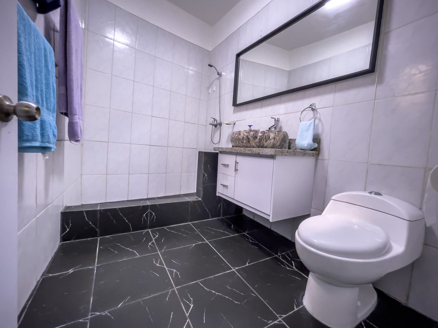 buyDRproperty Modern bathroom with black marble-style floor, white tiles, and a floating vanity. Sosua Real Estate