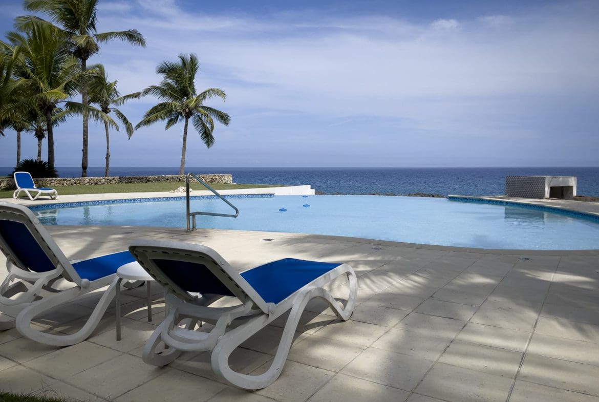 buyDRproperty Oceanfront pool with lounge chairs overlooking the ocean, near palm trees. Sosua Real Estate