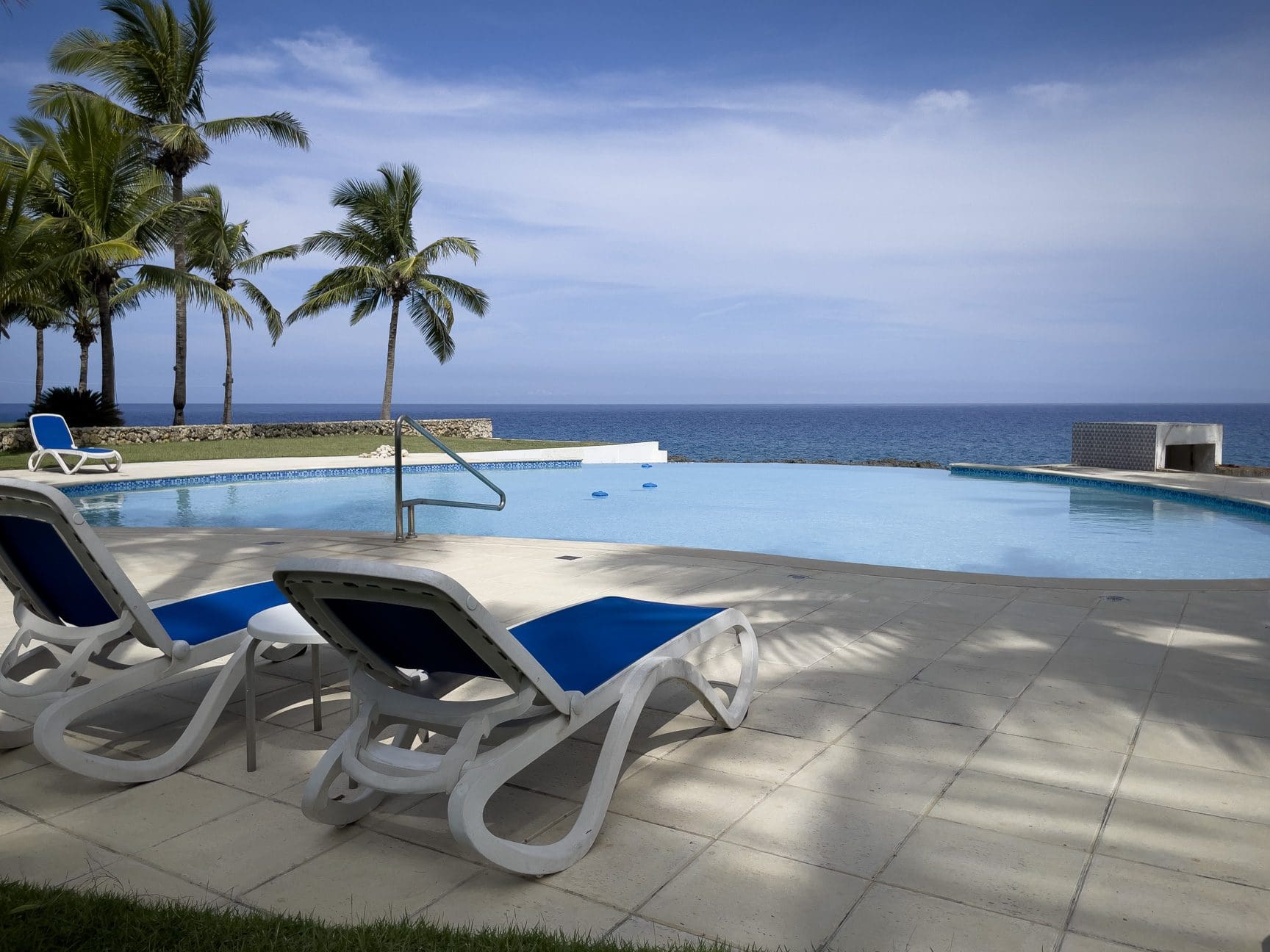 buyDRproperty Oceanfront pool with lounge chairs overlooking the ocean, near palm trees. Sosua Real Estate