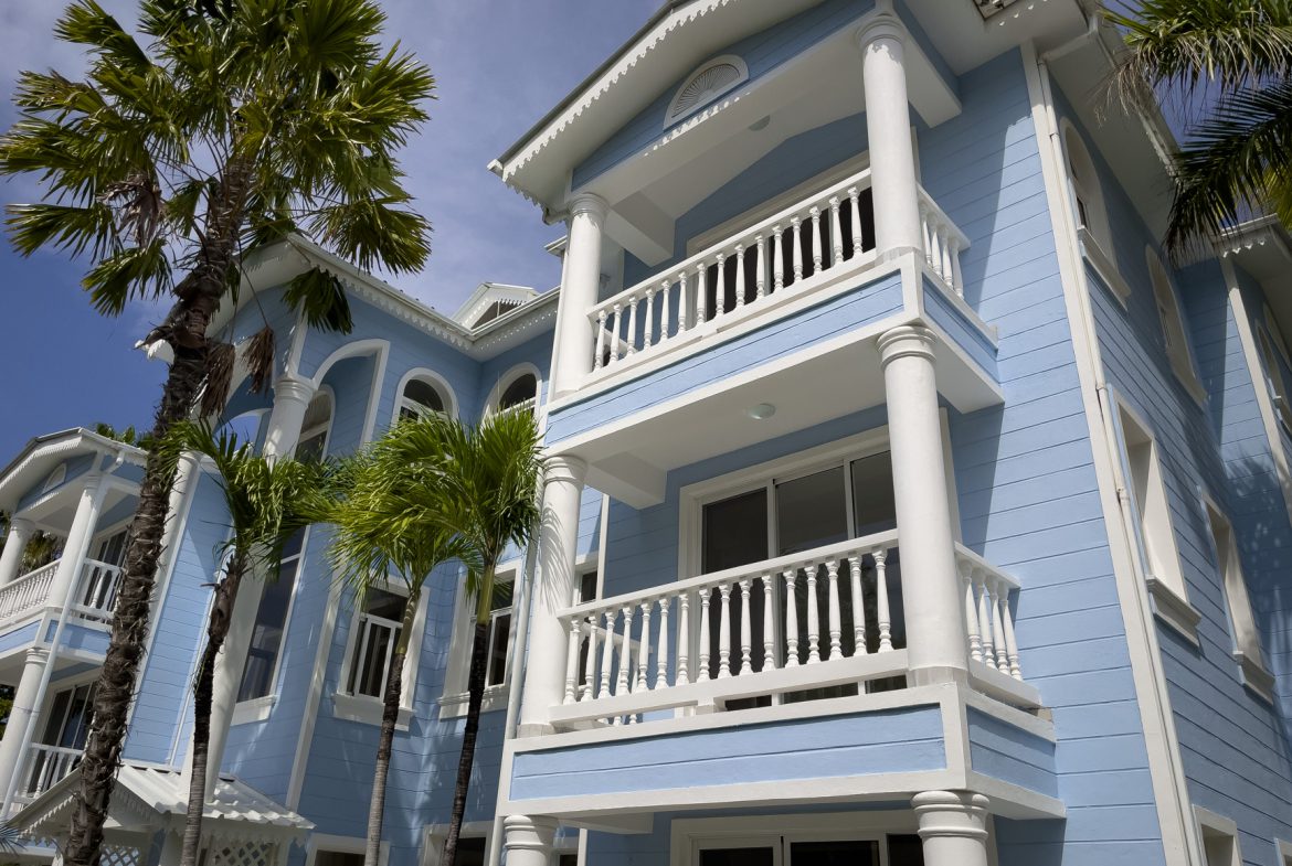 buyDRproperty Blue oceanfront condo with white pillars and balconies, palm trees. Sosua Real Estate