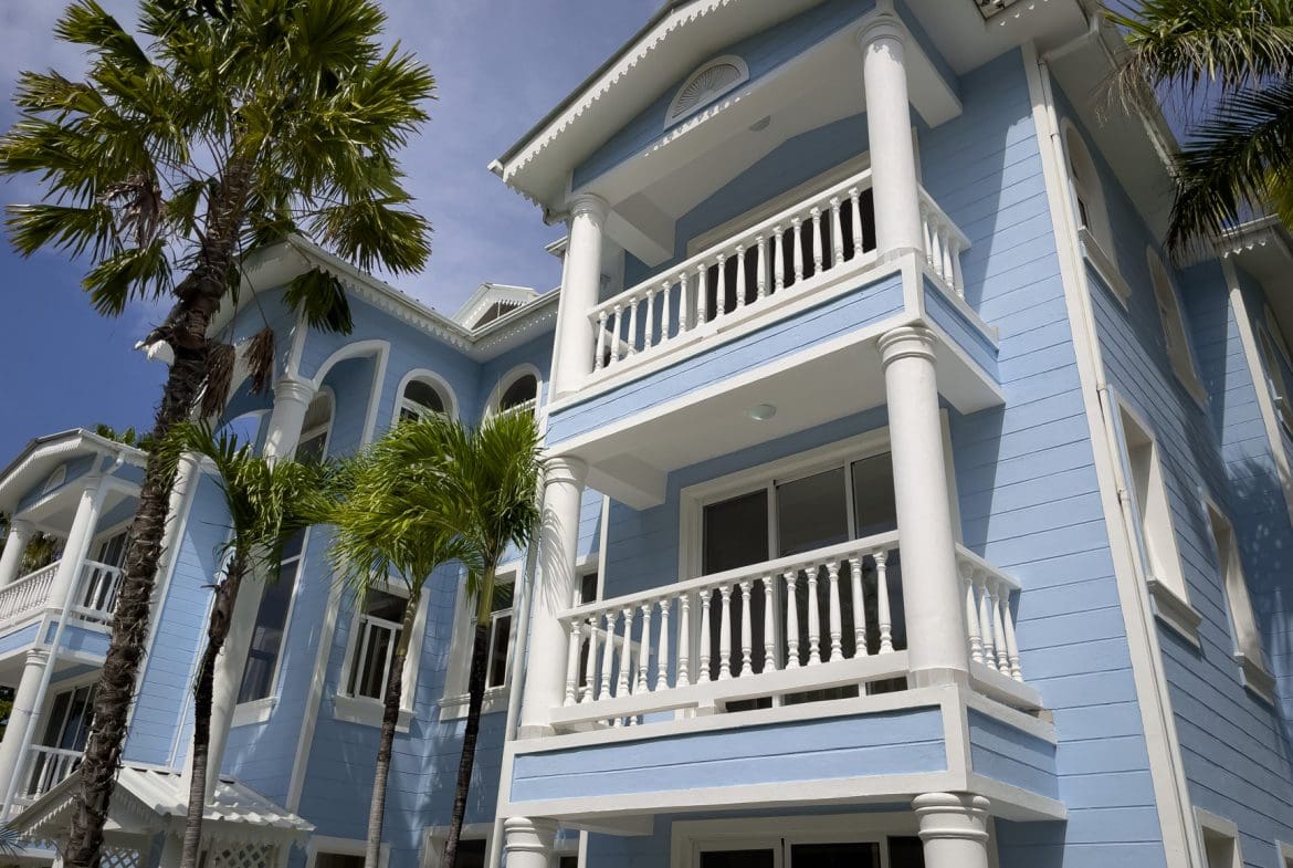 buyDRproperty Blue oceanfront condo with white pillars and balconies, palm trees. Sosua Real Estate