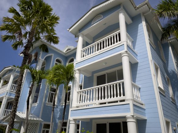 buyDRproperty Blue oceanfront condo with white pillars and balconies, palm trees. Sosua Real Estate