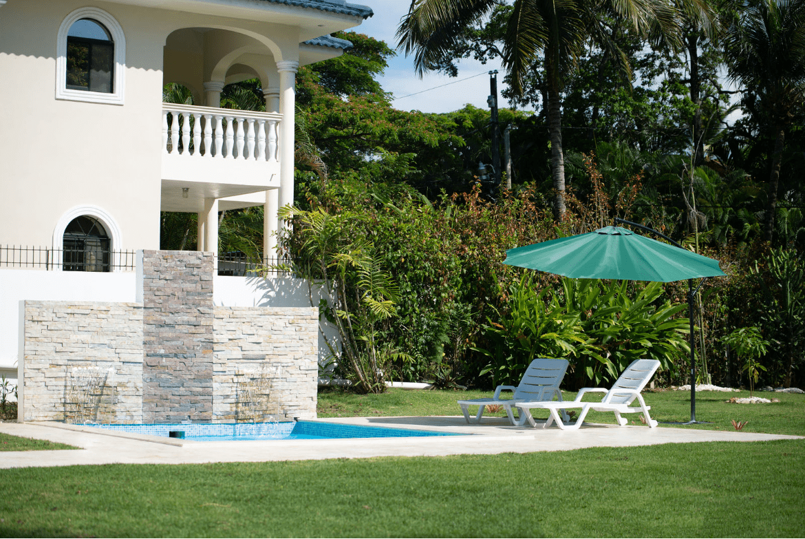 buyDRproperty Gorgeous 5 Bedroom Villa with pool and garden. Two lounge chairs under a green umbrella. Sosua Real Estate