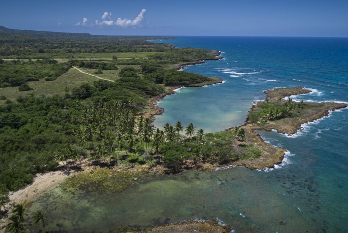 buyDRproperty Aerial view of oceanfront development property with marina potential, featuring a coastline, lush green vegetation, and clear blue waters. Sosua Real Estate