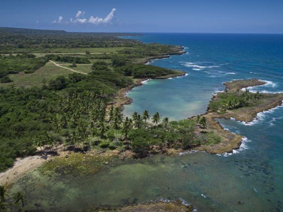 buyDRproperty Aerial view of oceanfront development property with marina potential, featuring a coastline, lush green vegetation, and clear blue waters. Sosua Real Estate