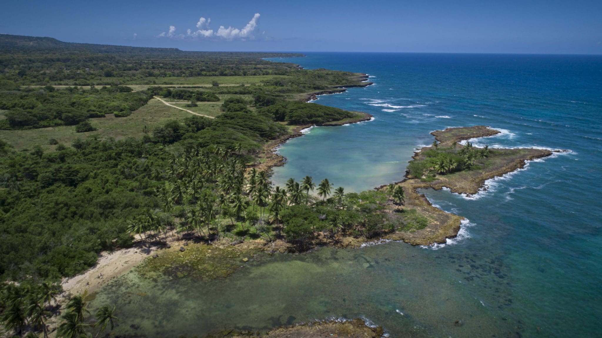 buyDRproperty Aerial view of oceanfront development property with marina potential, featuring a coastline, lush green vegetation, and clear blue waters. Sosua Real Estate