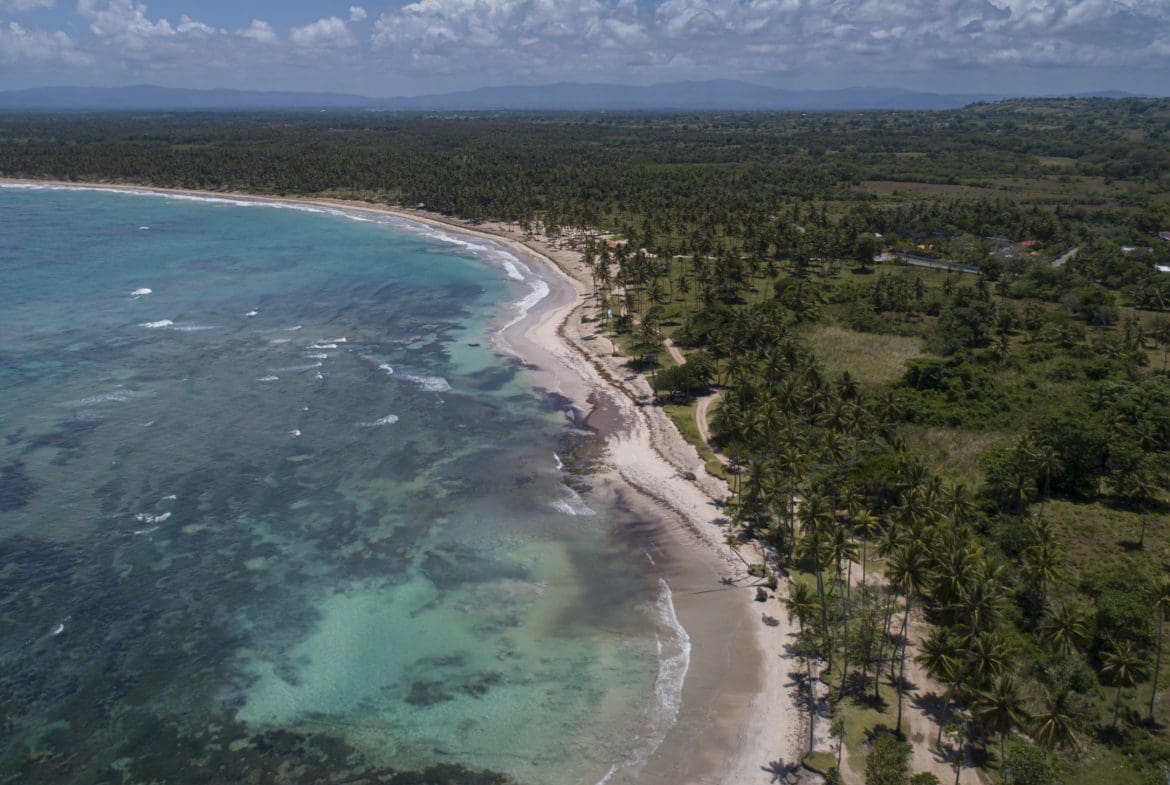 buyDRproperty Aerial view of a beautiful oceanfront development property with potential marina, featuring crystal clear turquoise waters and a sandy beach. Sosua Real Estate