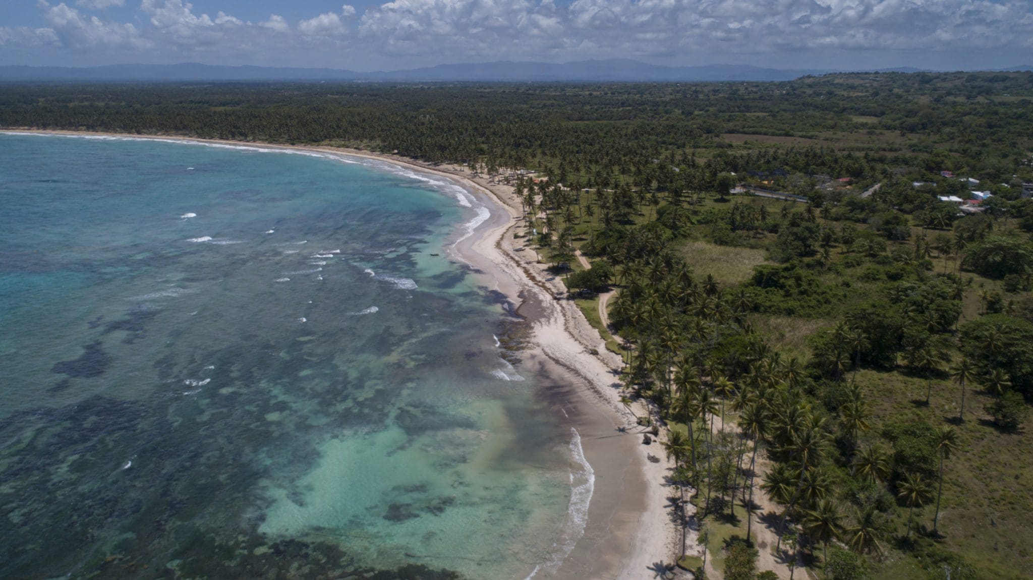 buyDRproperty Aerial view of a beautiful oceanfront development property with potential marina, featuring crystal clear turquoise waters and a sandy beach. Sosua Real Estate