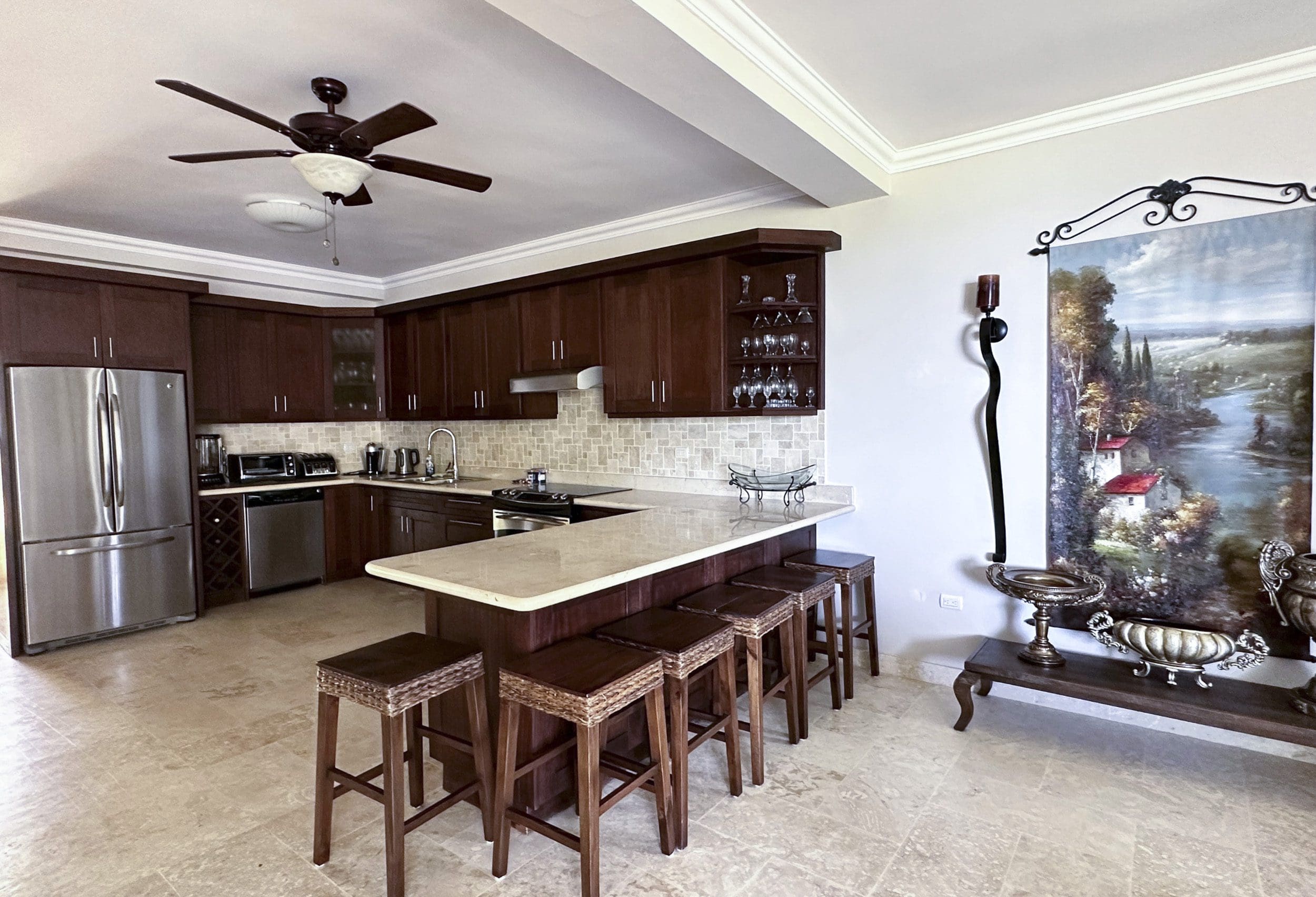 buyDRproperty Spacious kitchen with dark wood cabinets, breakfast bar, and stainless steel appliances in a Sosua condo. Sosua Real Estate