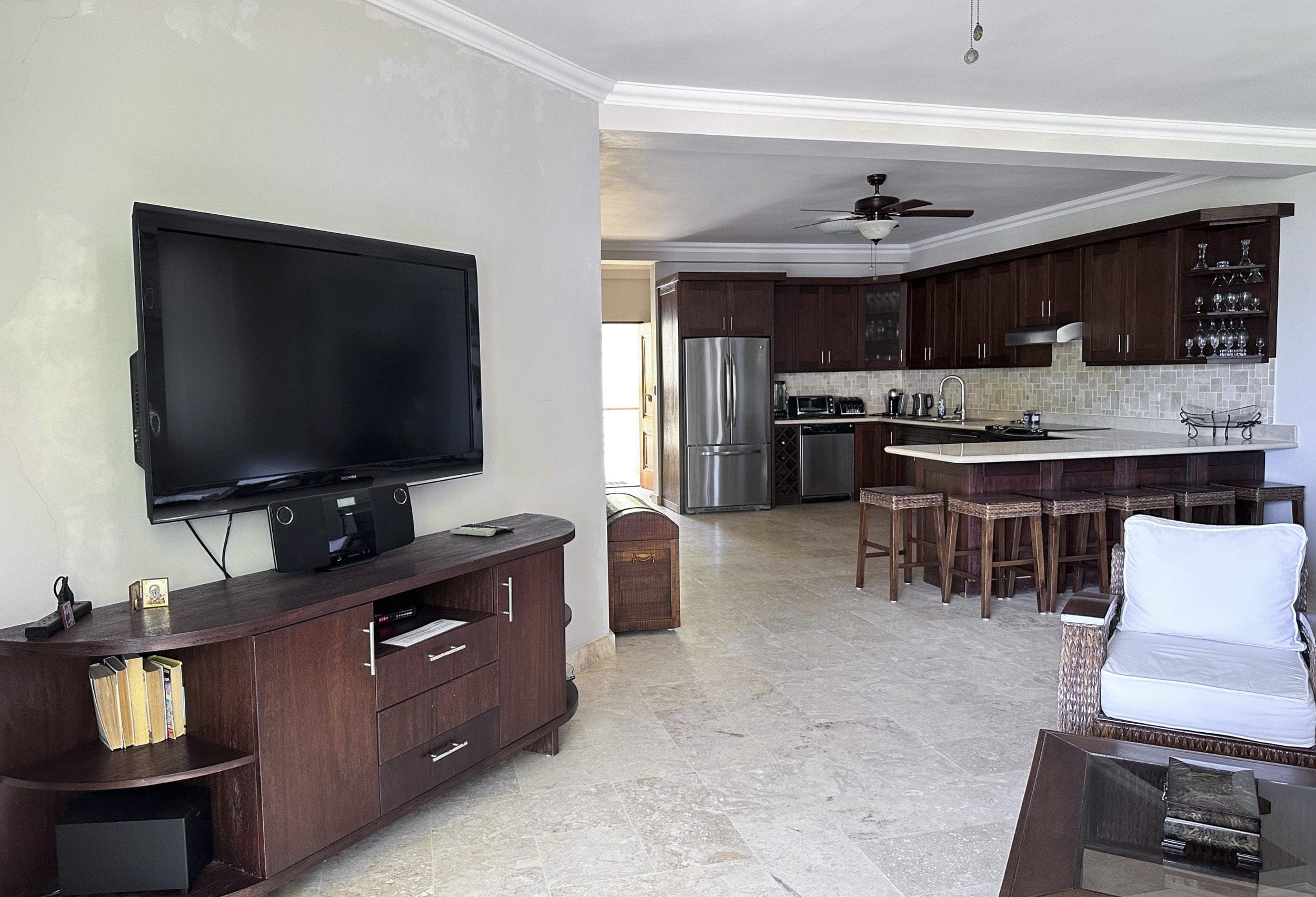 buyDRproperty Living room and kitchen in a 2-bedroom condo for sale in Sosua with dark wood cabinets and seating. Sosua Real Estate