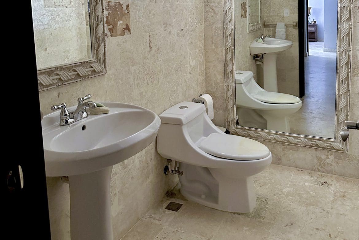 buyDRproperty Bathroom with pedestal sink, toilet, and mirror. Tile walls and floor, Sosua condo for sale. Sosua Real Estate