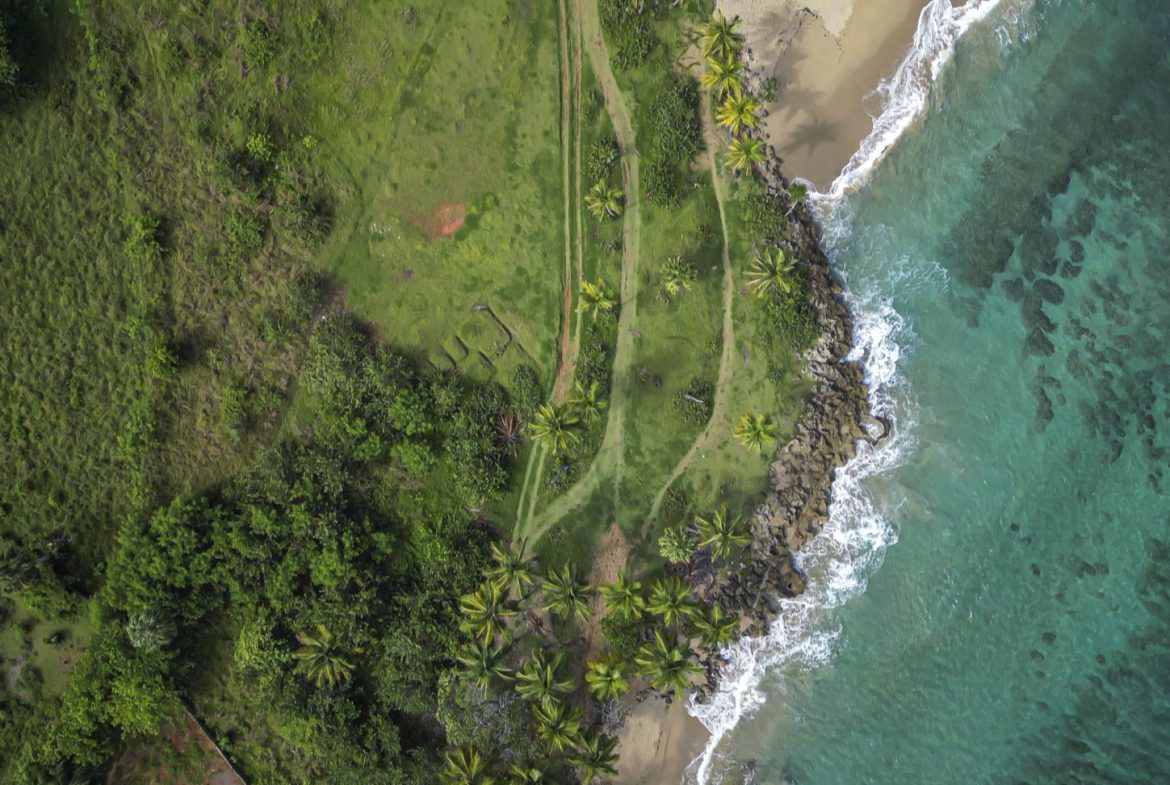 buyDRproperty Aerial view of stunning oceanfront development property with green grass and turquoise water. Sosua Real Estate