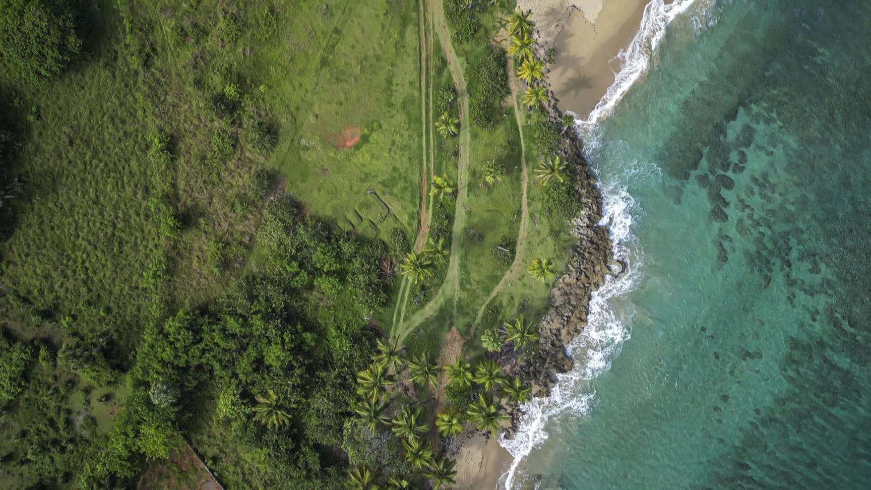 buyDRproperty Aerial view of stunning oceanfront development property with green grass and turquoise water. Sosua Real Estate
