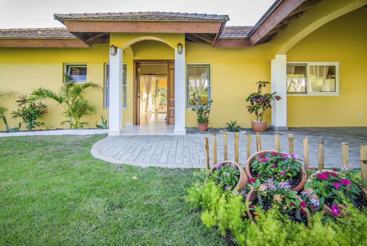 buyDRproperty Villa for sale in Terramar community with yellow exterior, lush landscaping and potted flowers. Sosua Real Estate