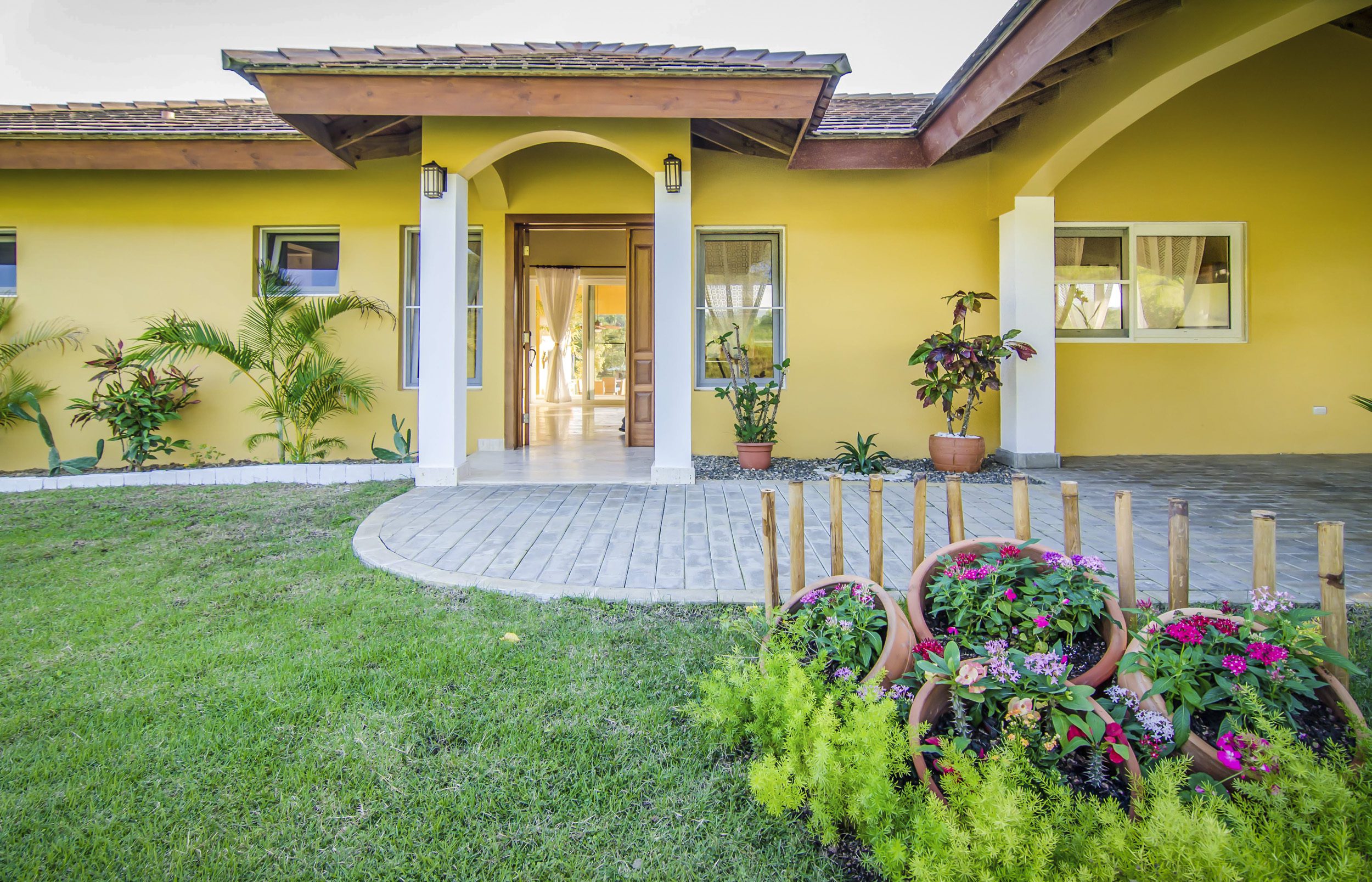 buyDRproperty Villa for sale in Terramar community with yellow exterior, lush landscaping and potted flowers. Sosua Real Estate