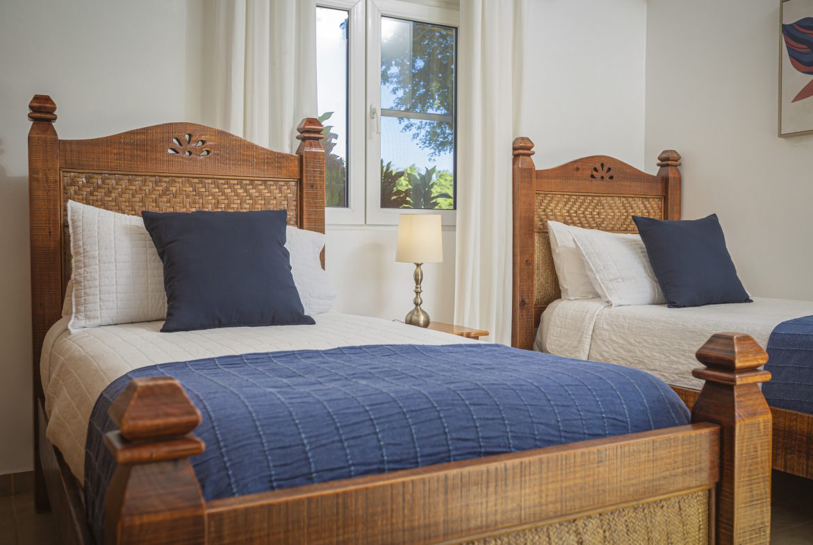 buyDRproperty Twin bedroom in a Villa For Sale. Beds with wooden frames, white bedding, and navy accents. Sosua Real Estate