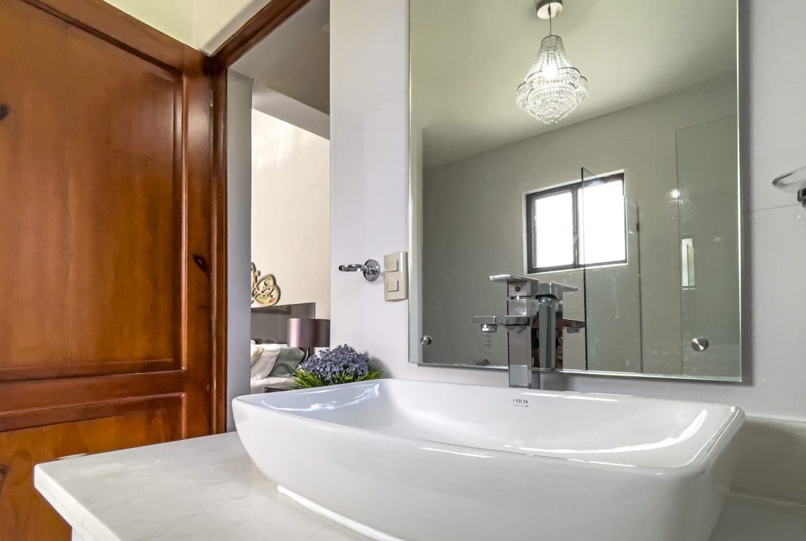buyDRproperty Modern bathroom with a white sink, chrome faucet, and a mirror reflecting a chandelier. Sosua Real Estate