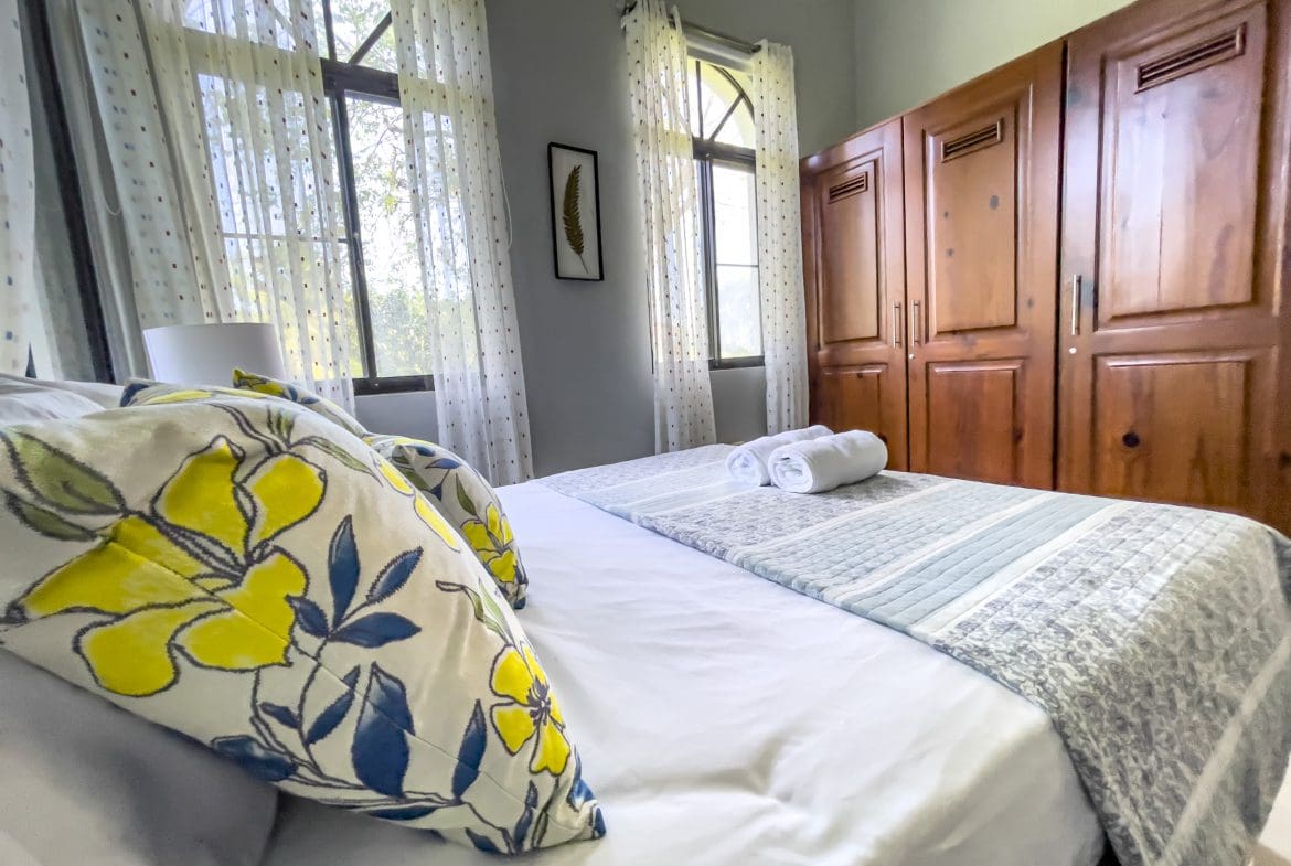buyDRproperty Cozy bedroom in a stunning 4 bedroom villa with floral pillows and wooden closet. Sosua Real Estate