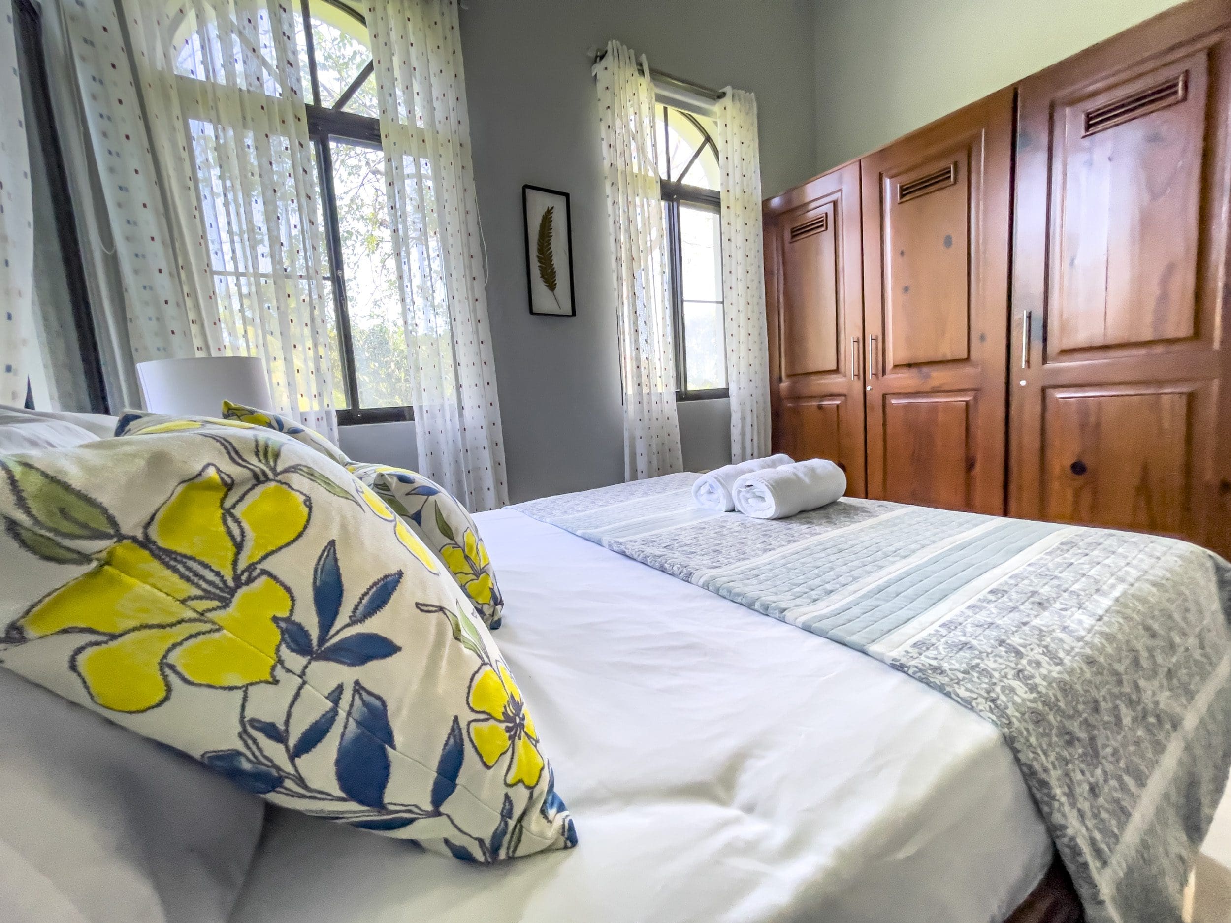 buyDRproperty Cozy bedroom in a stunning 4 bedroom villa with floral pillows and wooden closet. Sosua Real Estate