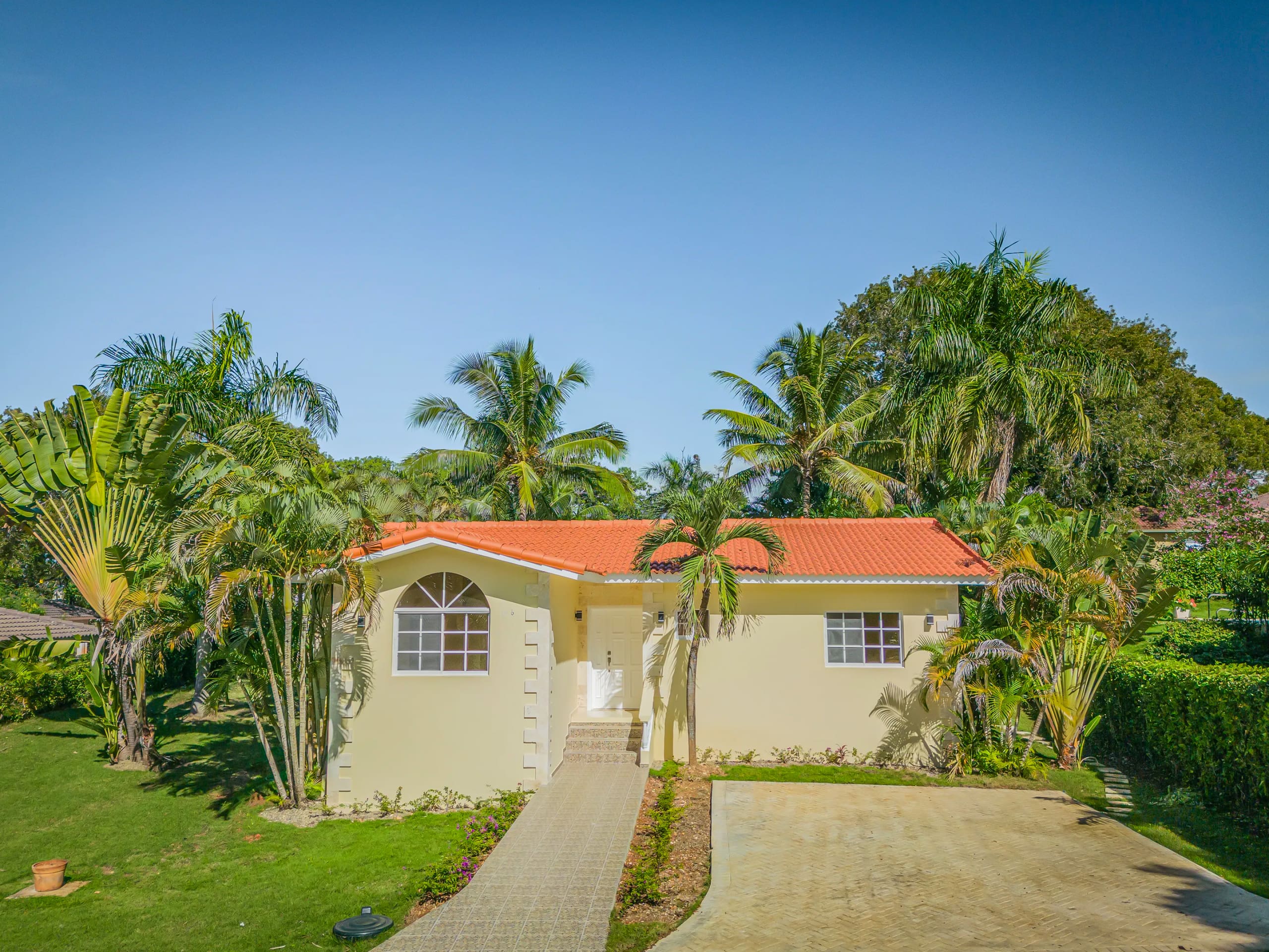 buyDRproperty Renovated Villa CAOBA in Residencial Hispaniola with lush tropical landscaping and red tile roof. Sosua Real Estate