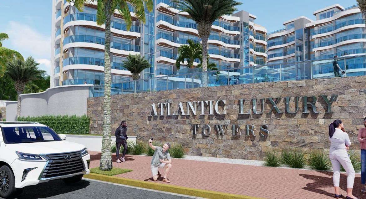 buyDRproperty Atlantic Luxury Towers in the Dominican Republic with people posing. The building sign reads "Atlantic Luxury Towers Sosua Real Estate