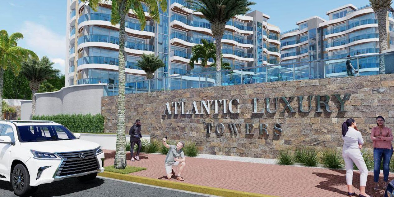 buyDRproperty Atlantic Luxury Towers in the Dominican Republic with people posing. The building sign reads "Atlantic Luxury Towers Sosua Real Estate
