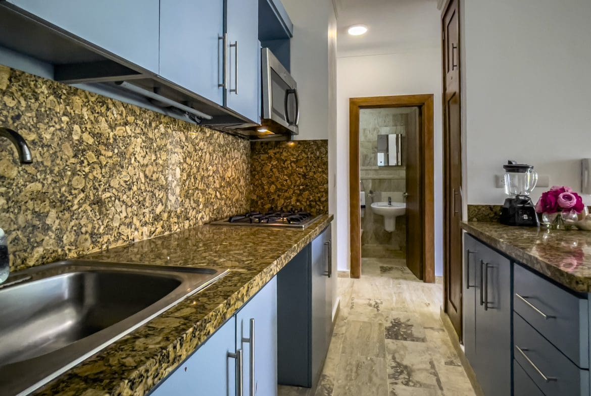 buyDRproperty Kitchen with blue cabinets, granite countertop, and view into bathroom in a 3 Bedroom Oceanfront Condo. Sosua Real Estate