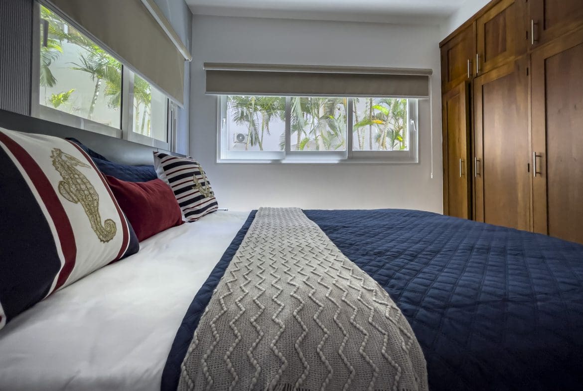 buyDRproperty Bedroom in a 3 Bedroom Oceanfront Condo with nautical-themed pillows and a view of palm trees. Sosua Real Estate