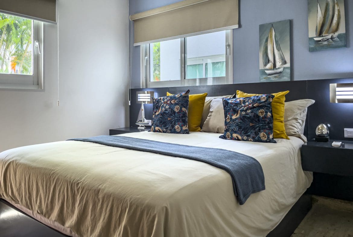 buyDRproperty Bedroom in a 3 Bedroom Oceanfront Condo with blue walls, art, and a cozy bed. Sosua Real Estate