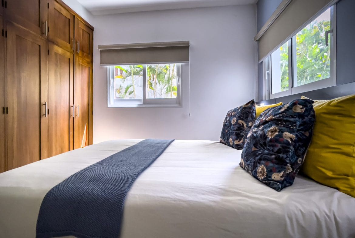 buyDRproperty Bedroom in a 3 Bedroom Oceanfront Condo with wooden wardrobe and blue and yellow pillows. Sosua Real Estate
