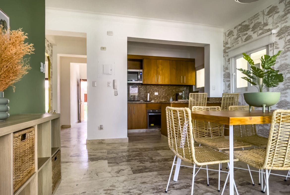 buyDRproperty Oceanfront condo for sale: dining area with table and chairs, kitchen with wooden cabinets. Sosua Real Estate
