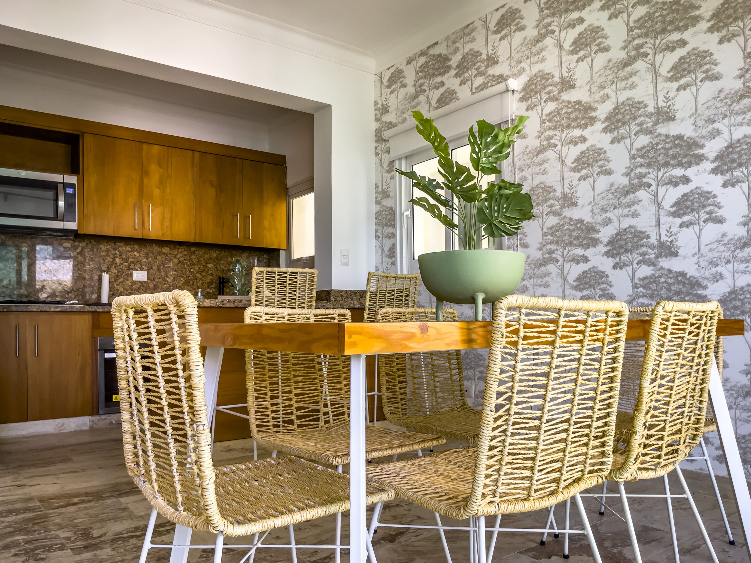 buyDRproperty Modern dining area with wooden table and woven chairs. Kitchen in background. Sosua Real Estate