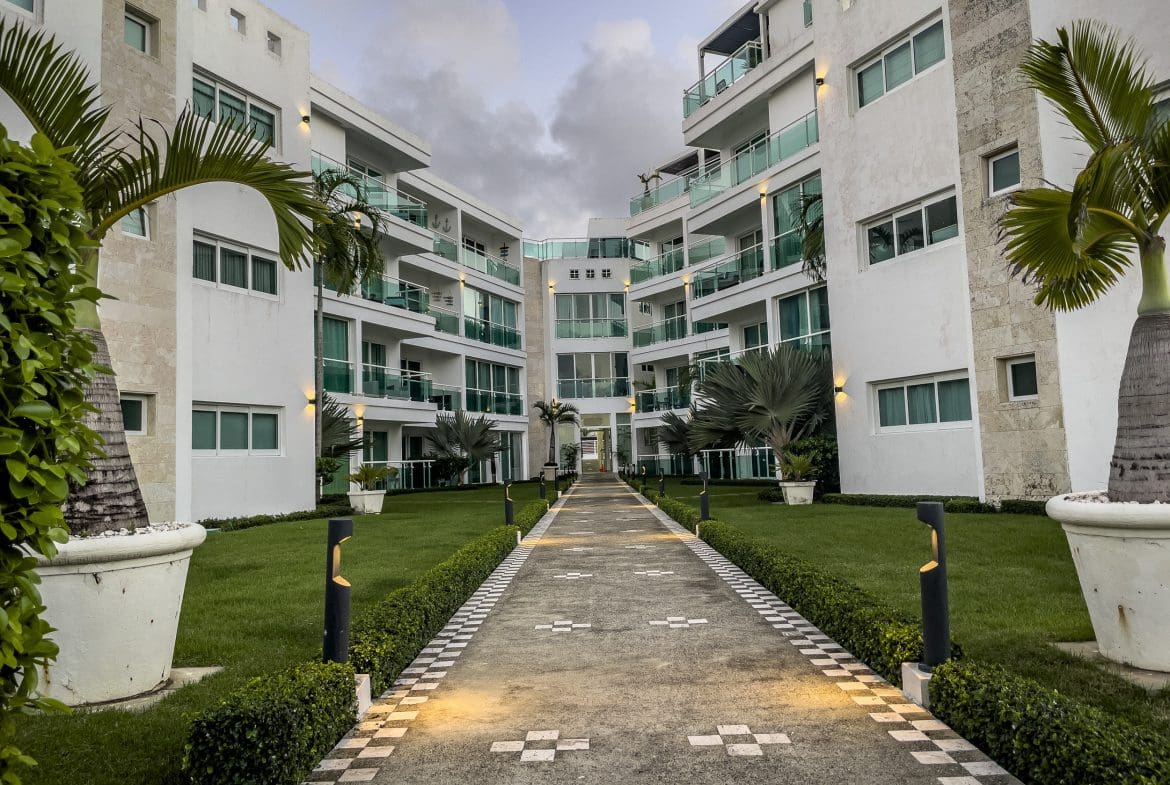buyDRproperty Modern 3 Bedroom Oceanfront Condo complex with walkway, palm trees, and green balconies. Sosua Real Estate