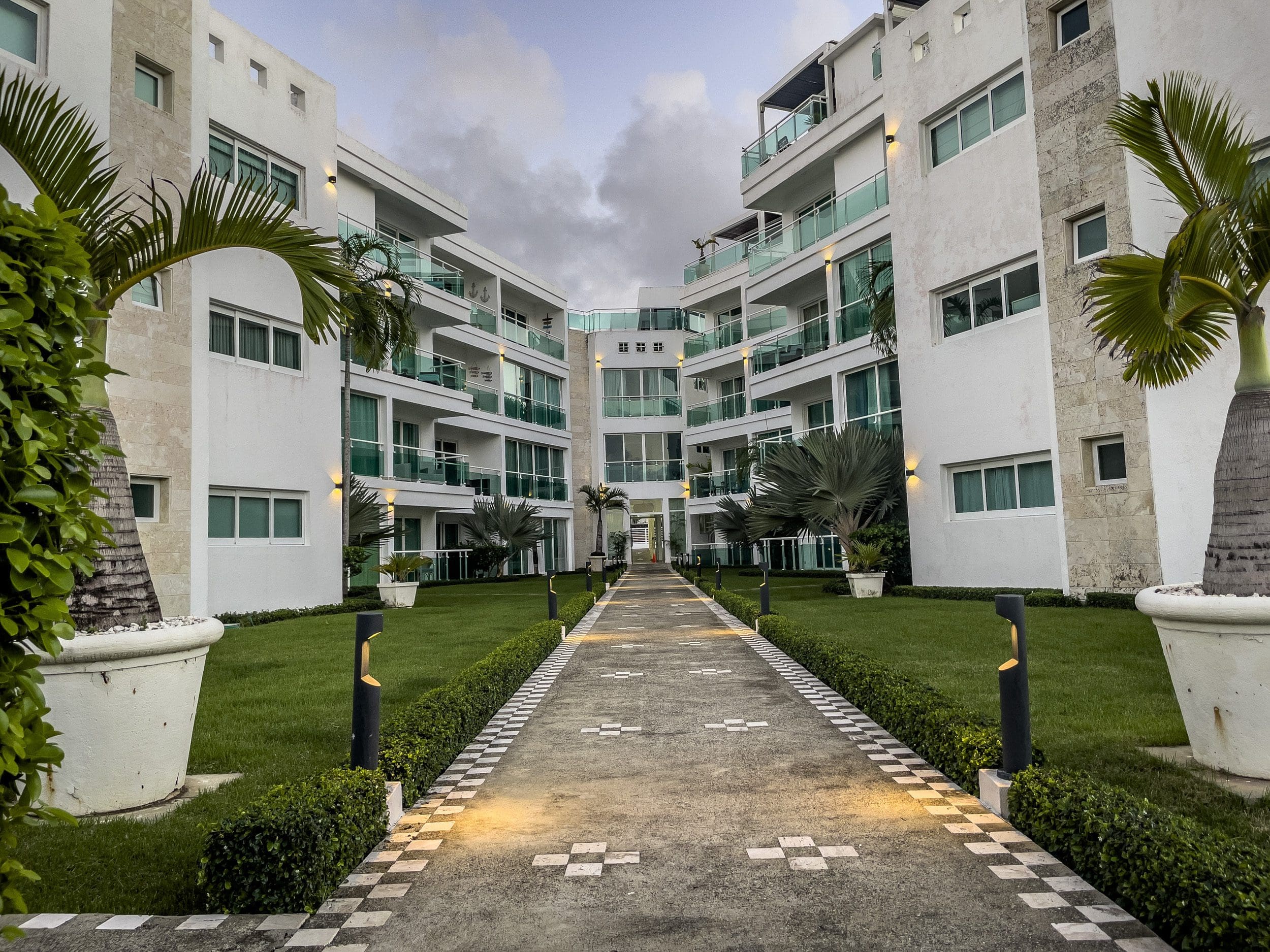 buyDRproperty Modern 3 Bedroom Oceanfront Condo complex with walkway, palm trees, and green balconies. Sosua Real Estate