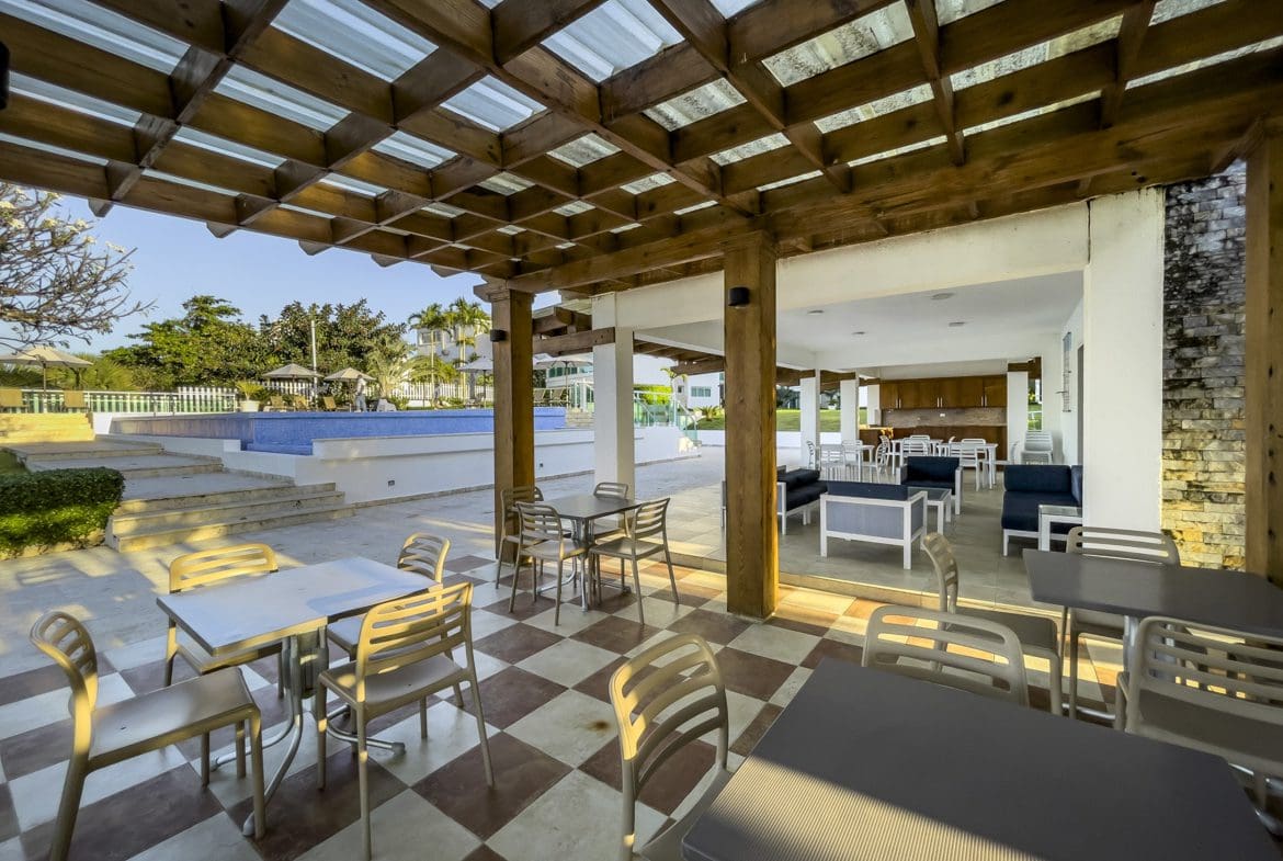 buyDRproperty Outdoor dining area with tables, chairs, and pool, possibly part of a 3 Bedroom Oceanfront Condo. Sosua Real Estate