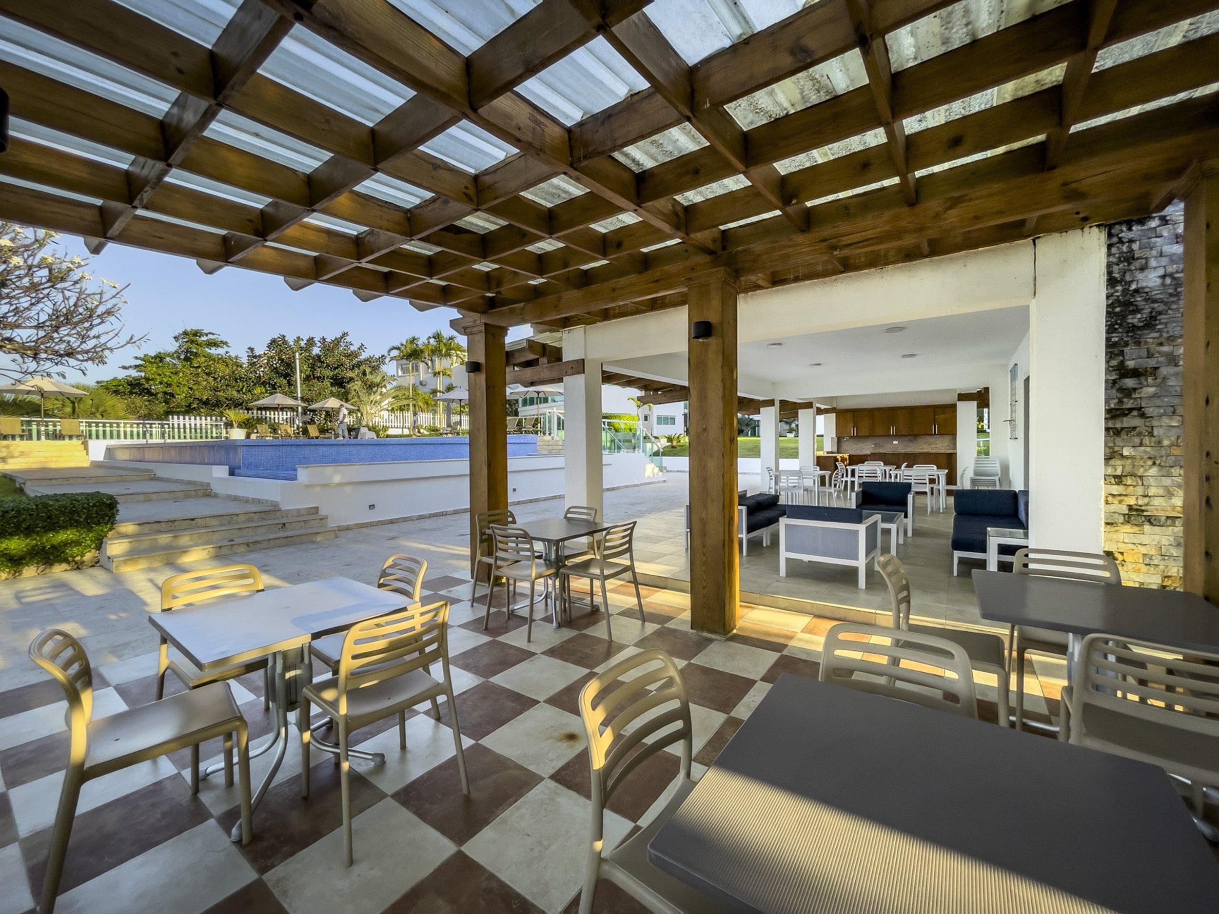 buyDRproperty Outdoor dining area with tables, chairs, and pool, possibly part of a 3 Bedroom Oceanfront Condo. Sosua Real Estate