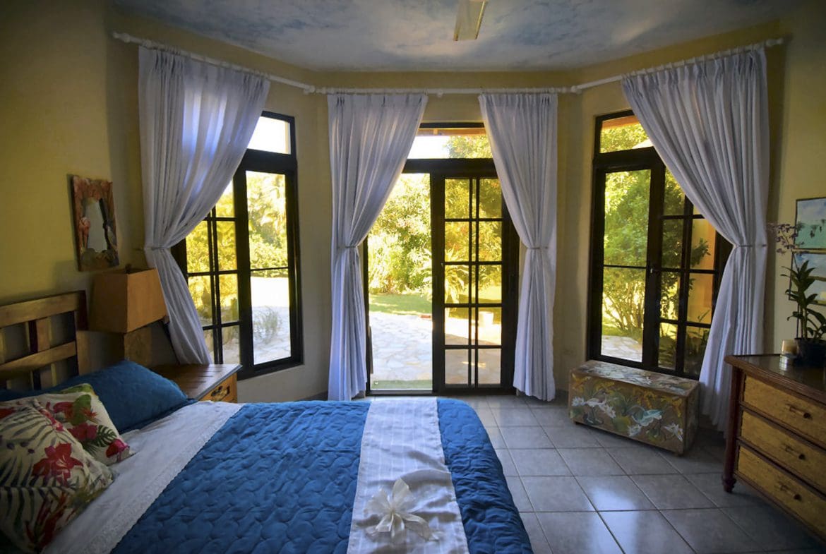 buyDRproperty Bedroom in a Beautiful 4 Bedroom Villa in Sosua with large windows, white curtains, and a view of the yard. Sosua Real Estate