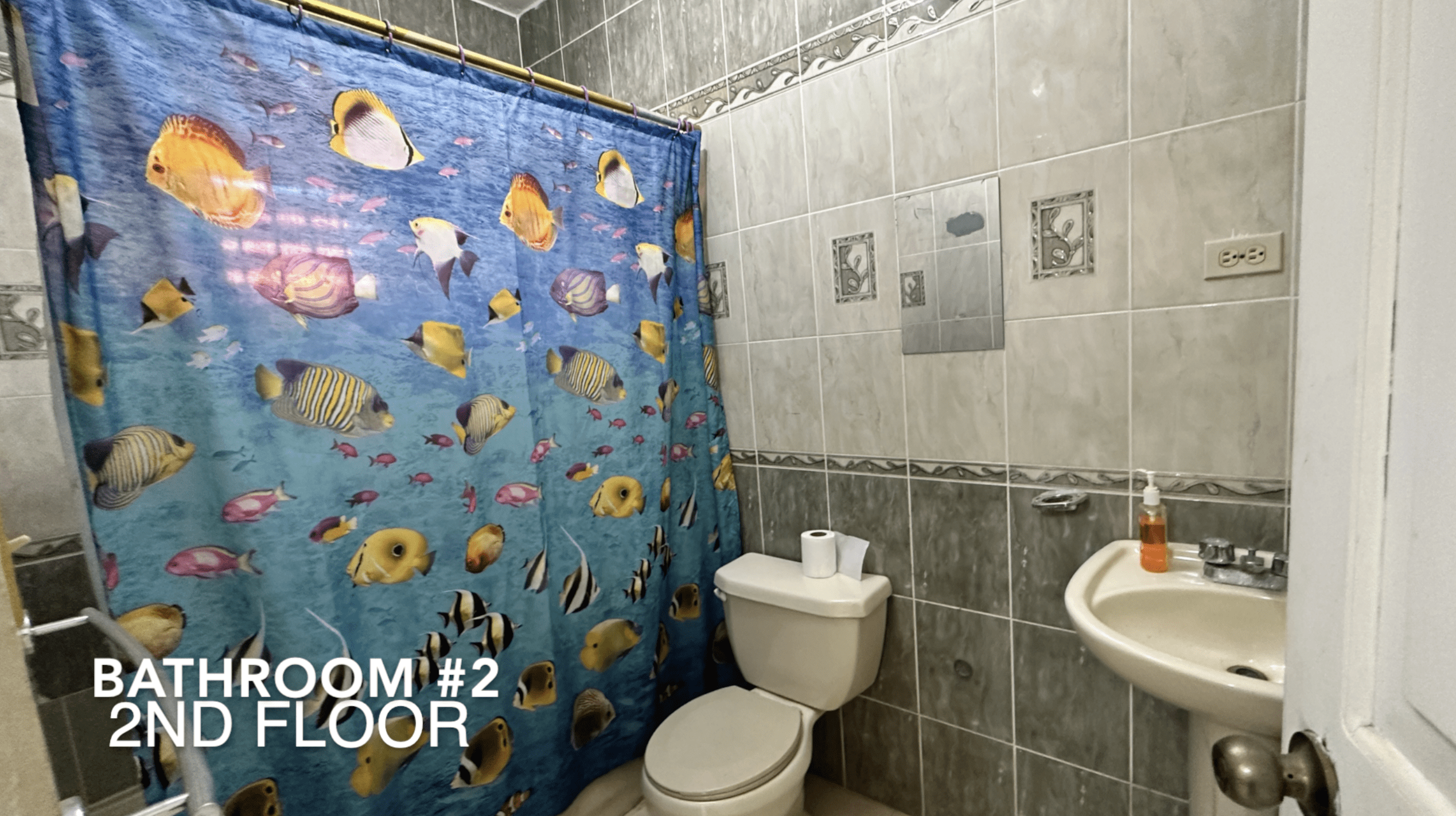 buyDRproperty Bathroom with fish-themed shower curtain. Text: Bathroom #2 2nd Floor. Part of the affordable hotel facility. Sosua Real Estate