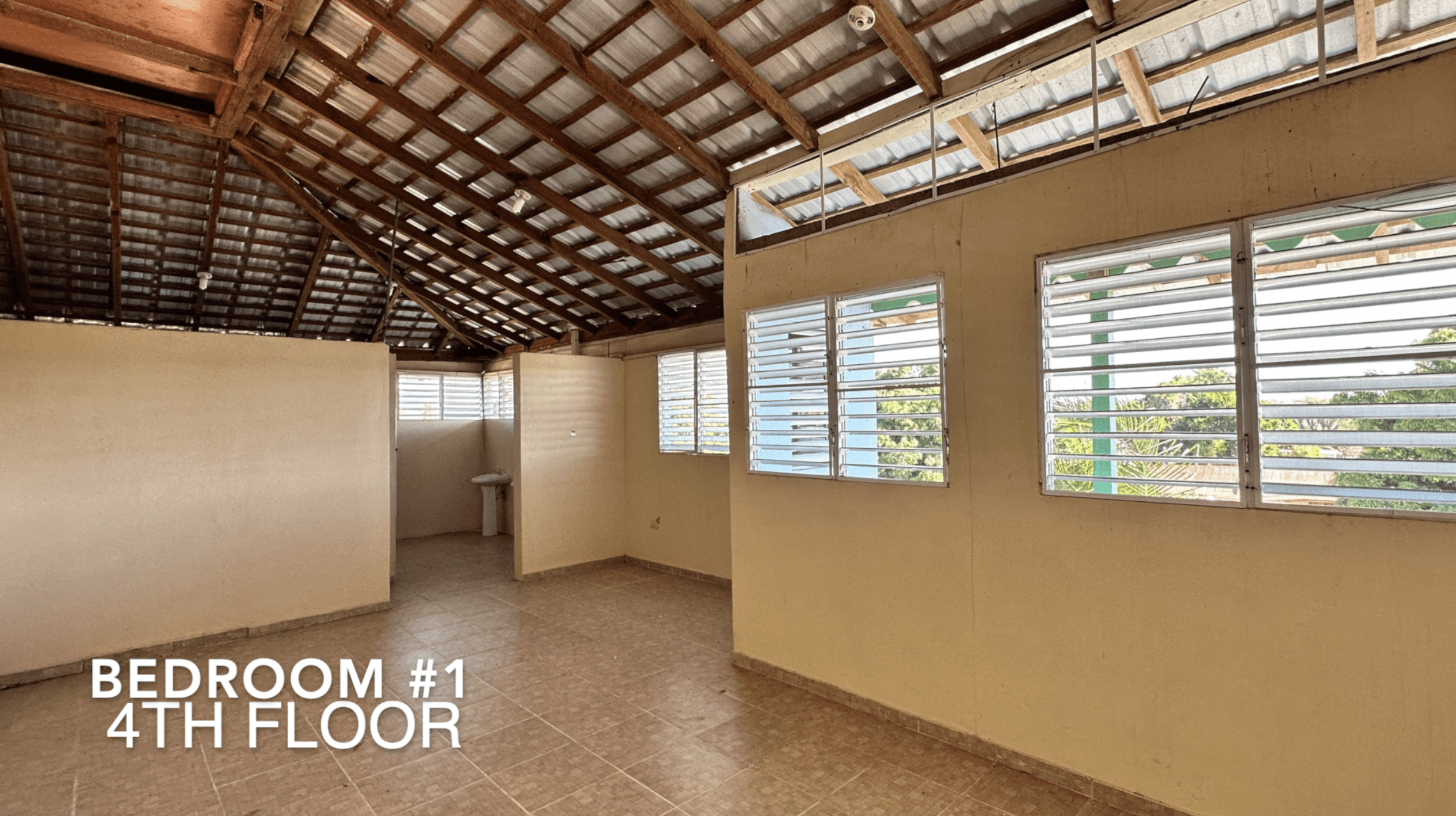 buyDRproperty Bedroom interior with high ceiling and windows, part of an affordable hotel facility. Sosua Real Estate