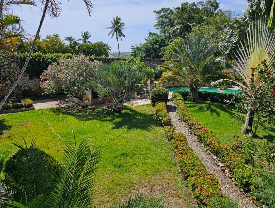 buyDRproperty Lush tropical garden at a hotel near the beach, with a pool and palm trees. Sosua Real Estate