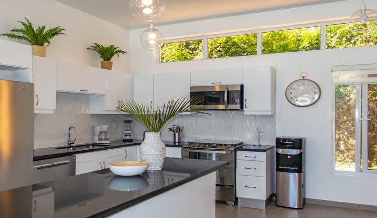 buyDRproperty Modern kitchen in a Beautiful Villa SUNBREEZE with white cabinets, dark countertop, and stainless steel appliances. Sosua Real Estate
