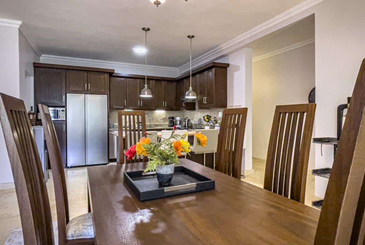 buyDRproperty Dining room with a wooden table and chairs, leading to the kitchen in a 3 Bedroom Oceanfront Condo. Sosua Real Estate