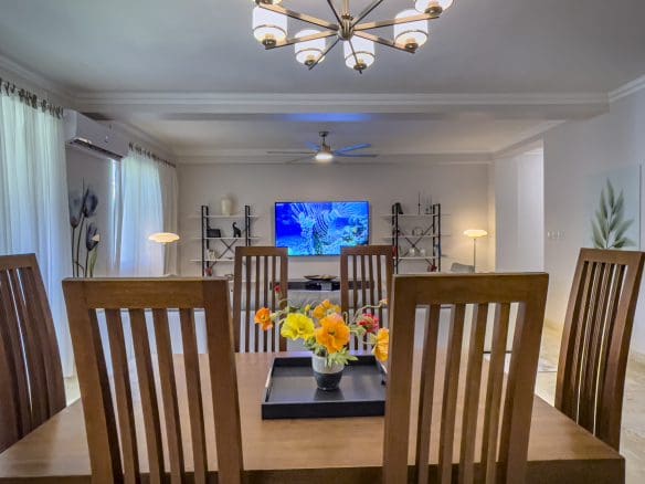 buyDRproperty Dining room of a 3 Bedroom Oceanfront Condo with wooden table and chairs, flowers, and a TV. Sosua Real Estate