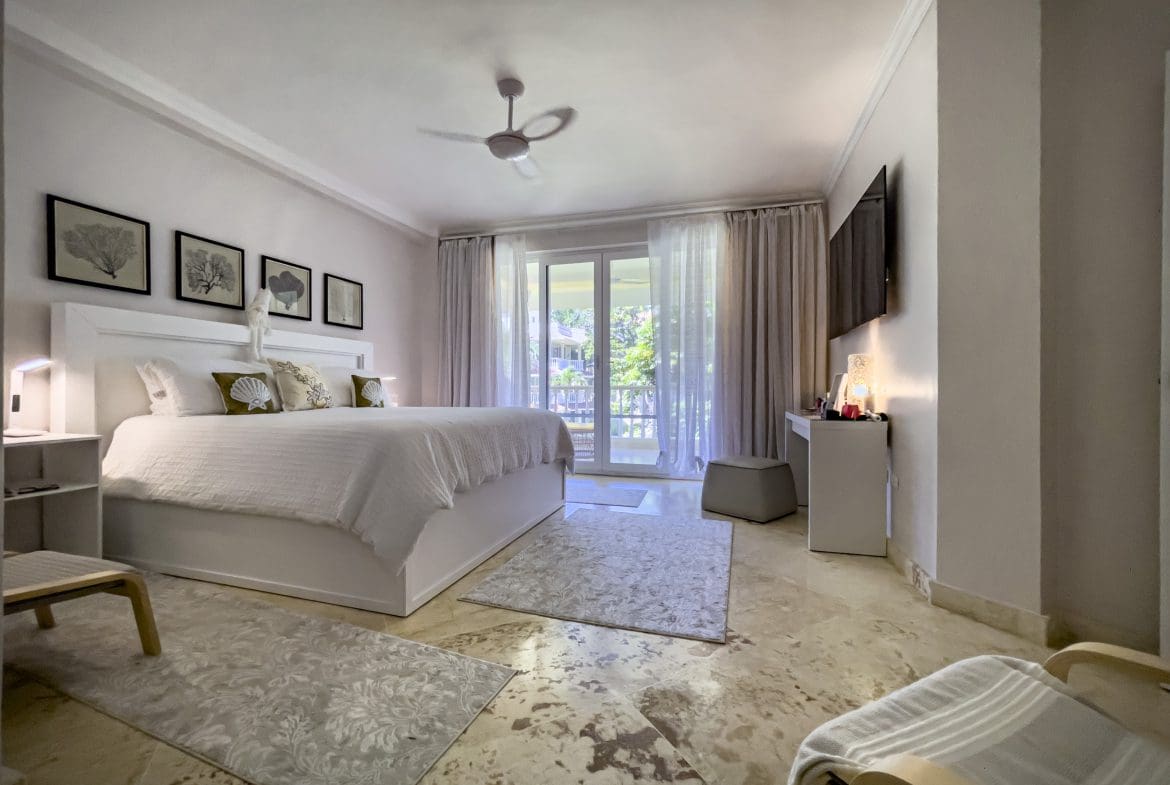 buyDRproperty Spacious bedroom in a 3 Bedroom Oceanfront Condo. Features a large bed, rugs, and balcony access. Sosua Real Estate