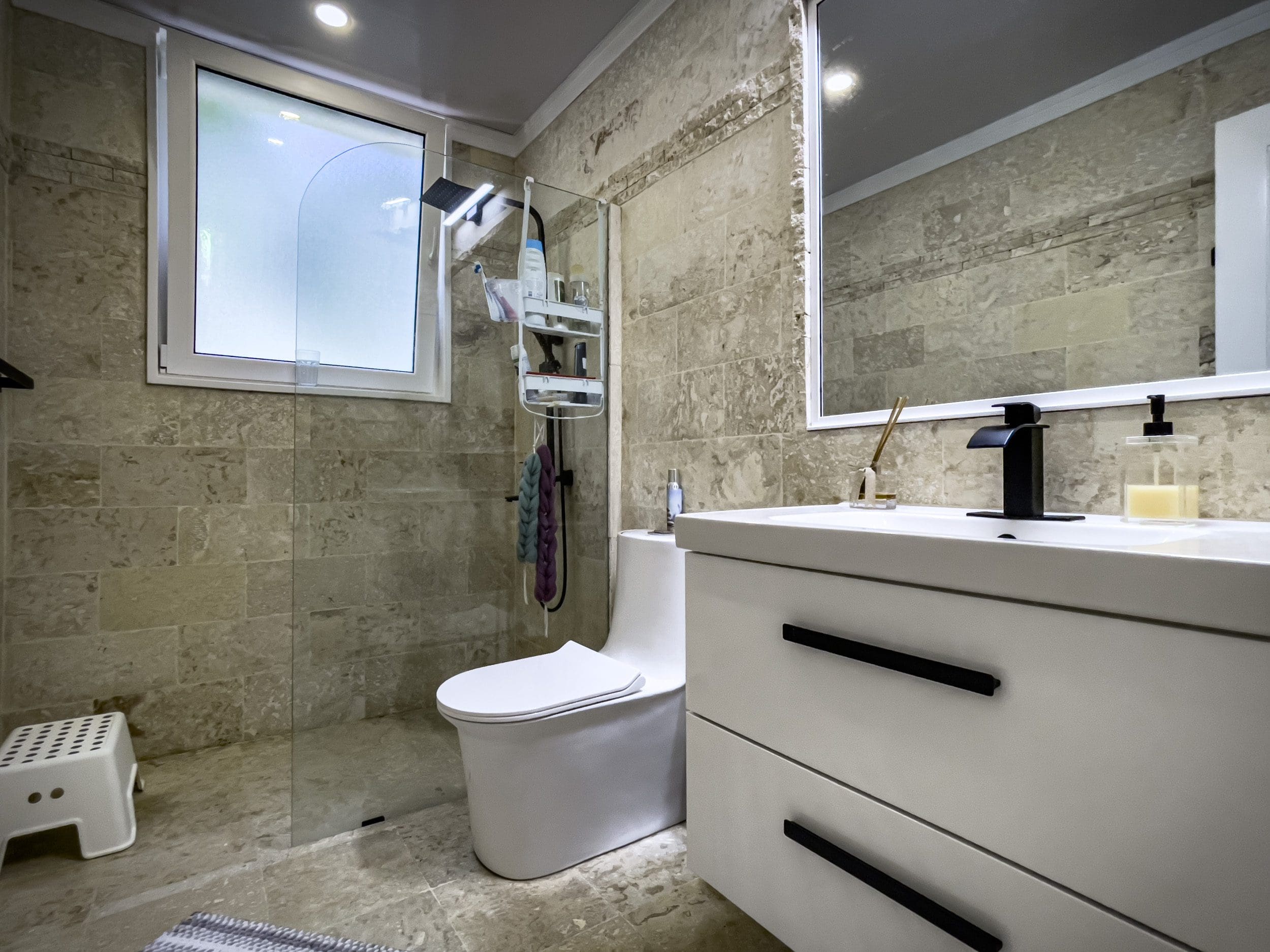 buyDRproperty Modern bathroom in a 3 Bedroom Oceanfront Condo with beige stone tiles, white toilet, and black faucet. Sosua Real Estate