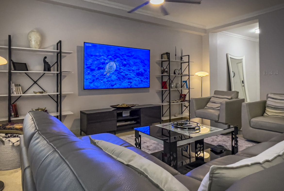 buyDRproperty Living room of a 3 bedroom oceanfront condo with a large TV and comfortable seating. Sosua Real Estate
